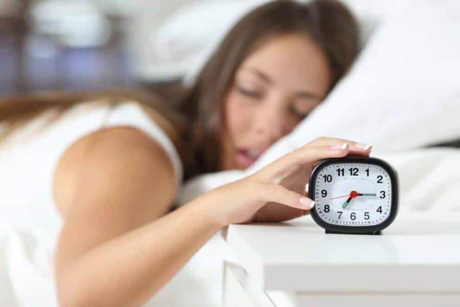 Woman in bed with hand on alarm clock