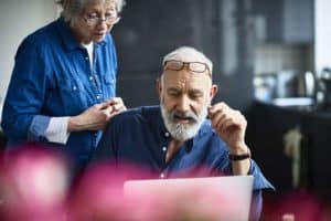 Hipster senior man with beard using laptop and woman watching