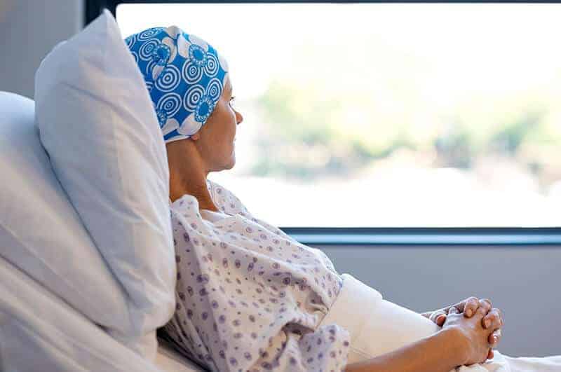 woman in hospital bed peers out window.