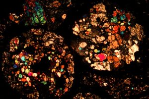 A meteorite thin section under a microscope. Different colors represent different minerals, because light travels through them in different ways. The round mineral aggregates are chondrules, which are a major component in primitive meteorites.