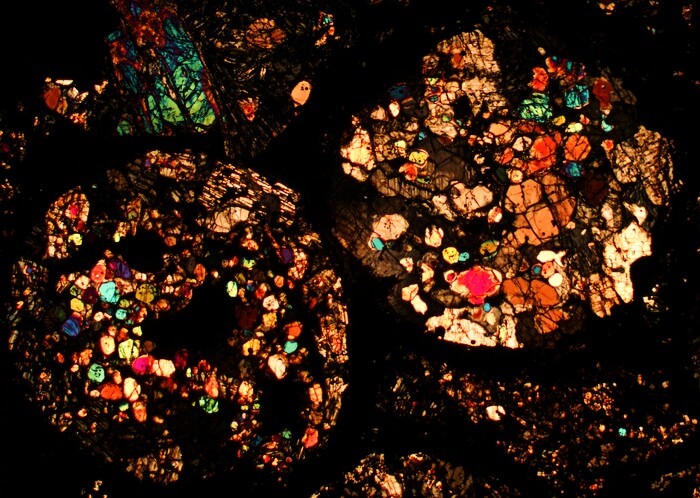 A meteorite thin section under a microscope. Different colors represent different minerals, because light travels through them in different ways. The round mineral aggregates are chondrules, which are a major component in primitive meteorites.