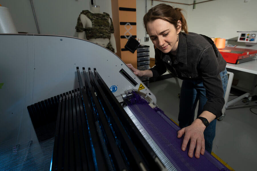 At Lincoln Laboratory’s Defense Fabric Discovery Center, Erin Doran demonstrates how reflective fibers can be woven into textiles. Such fibers could function as indelible, scannable labels to easily sort fabrics for recycling.