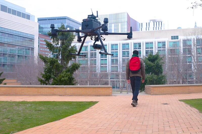 Student walking across campus followed by a drone