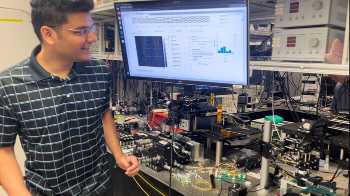 Researchers have developed a new light-based computing scheme called LightHash that reduces the energy necessary for cryptocurrency and blockchain applications. First author Sunil Pai is pictured with the optical setup used for the new research.