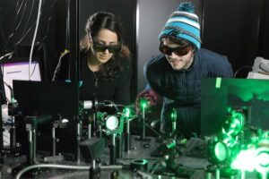 Doctoral candidates Sara Makarem Hoseini and Daniel Hirt observe the plasma ray setup. Though Hirt wears a knit cap and puffy jacket for effect, the cooling is localized and doesn’t have much influence on the surrounding room temperature.