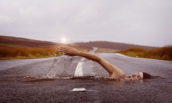 Dream-like image of a person swimming acorss an asphalt road