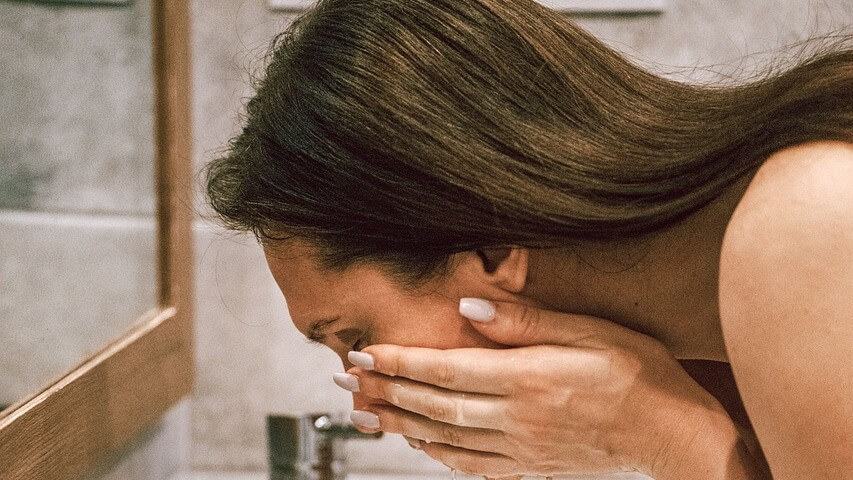 Woman rinsing her face in a bathroom sink. Pixabay