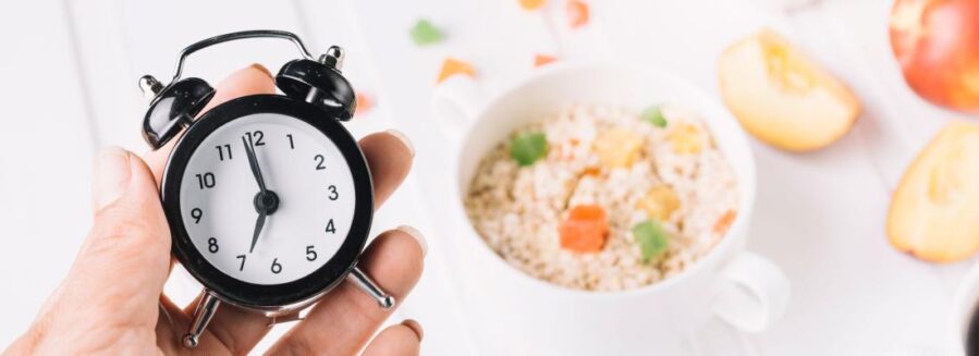 A hand holding a small clock in front of a meal