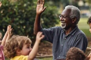 a healthy senior adult smiling and waving to a group of young children (aged 2-5) playing together