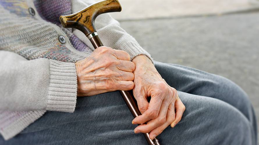 elderly man sitting on a bench with cane in hands