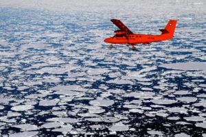A BAS Twin Otter flies over Antarctic sea ice.