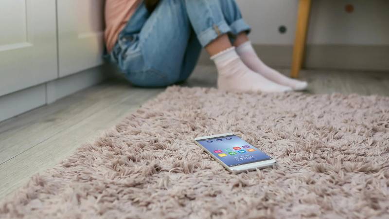 Female sittingon floor afraid of her phone which is on the carpet near her