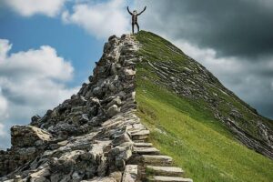 Concept: A split image divided down the middle. Left Side: A person triumphantly climbing a mountain peak, with a clear blue sky and sunshine. This represents the stereotypical image of success following failure. Right Side: A person carefully navigating a rocky, uneven path at the base of a mountain. The sky is overcast with some storm clouds. This depicts the reality of setbacks and challenges that come with overcoming failure.