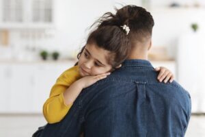 Sad looking girl held by a man, likely her father