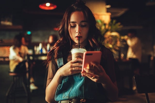 Woman looking at her phone and sipping a cold drink through a straw