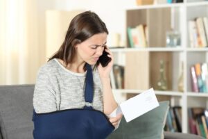 woman with arm in sling on phone looking at bill