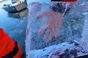 A hand can be seen through a clear block of black lake ice