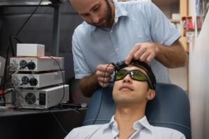 Caltech postdoctoral scholar Simon Mahler, a co-lead author of the new paper, is shown here placing the CSOS device on the head of graduate student Yu Xi Huang, the other co-lead author of the paper. The new device is affordable and compact, making it ideal for stroke assessment in a clinical setting.