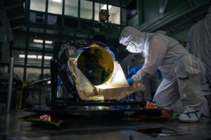 The prototype LISA telescope undergoes post-delivery inspection in a darkened NASA Goddard clean room on May 20. The entire telescope is made from an amber-colored glass-ceramic that resists changes in shape over a wide temperature range, and the mirror’s surface is coated in gold.