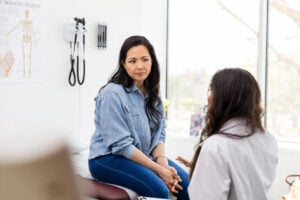 The mid adult woman becomes serious as the unrecognizable female doctor gives her some unwelcome news.