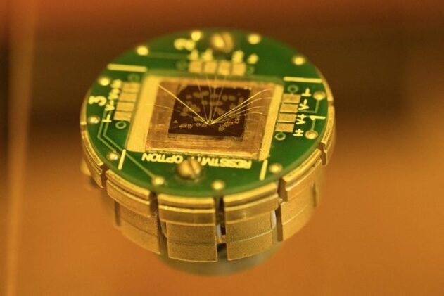 Chalmers researchers have developed tiny memory devices using a novel, atomically thin material, visible as clusters of golden dots on the chip surface. The material combines two opposing magnetic forces, generating an exchange force and a tilted overall magnetic alignment. This unusual coexistence could simplify device fabrication while reducing energy use in memory devices by a factor of ten, offering major benefits for future computers, artificial intelligence, and advanced data processing.
