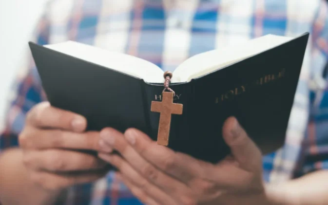 Hands holding an open Bible with crucifix bookmark