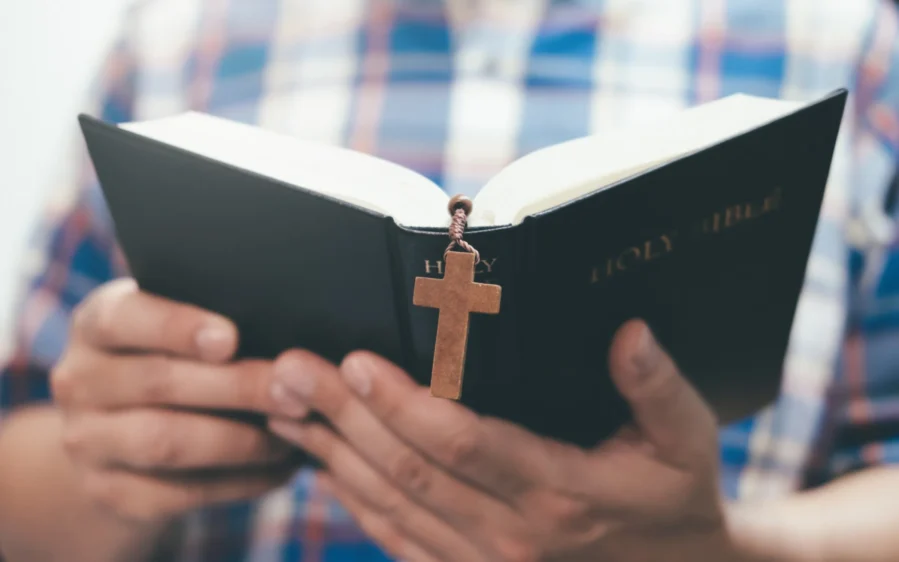 Hands holding an open Bible with crucifix bookmark