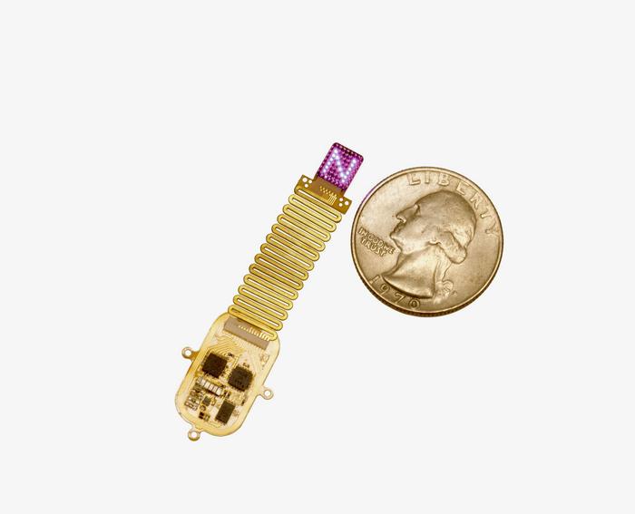 The thin, flexible, wireless device sits next to a quarter for scale. Device emits complex patterns of light (shown here as an "N") to transmit information directly to the brain.