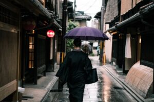 Japanese woman in traditional dress walking with umbrella in the rain