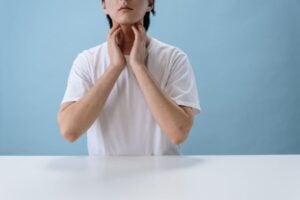 An Asian young man placing his fingers on either side of his throat