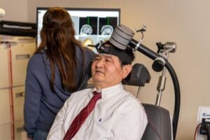 Xingbao Li, M.D., demonstrates how someone would receive rTMS therapy to reduce nicotine cravings. Photo by Clif Rhodes