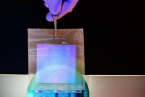 A freestanding sheet of single‑crystalline silicon nanomembrane is held above a silicon wafer patterned with its first layer of electronic circuits.