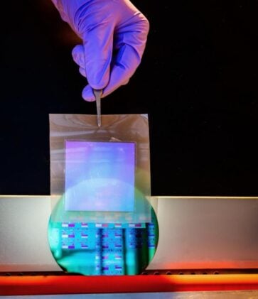 A freestanding sheet of single‑crystalline silicon nanomembrane is held above a silicon wafer patterned with its first layer of electronic circuits.