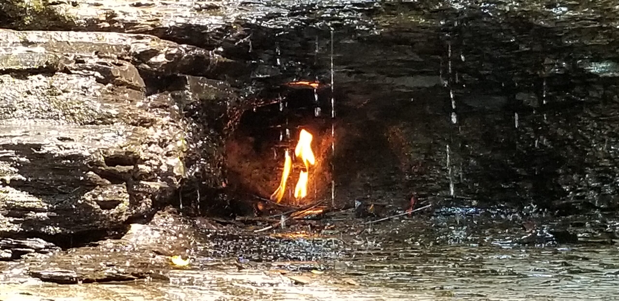 Small natural gas flame glowing behind falling water at Eternal Flame Falls in western New York