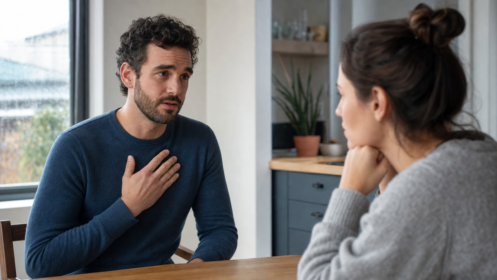 A man with one hand over his chest speaking carefully to a woman across a kitchen table