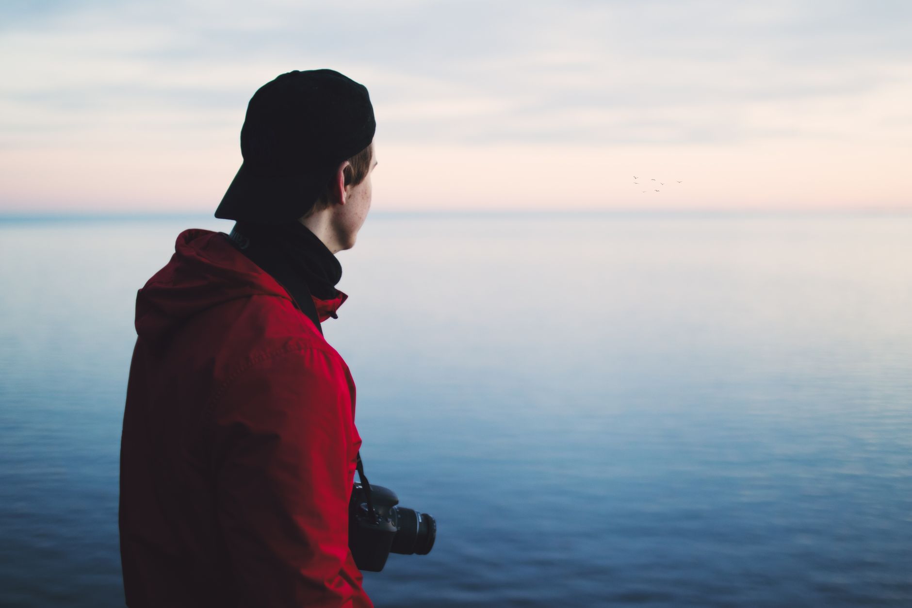 A man with a camera looking across a calm ocean under a pastel sky