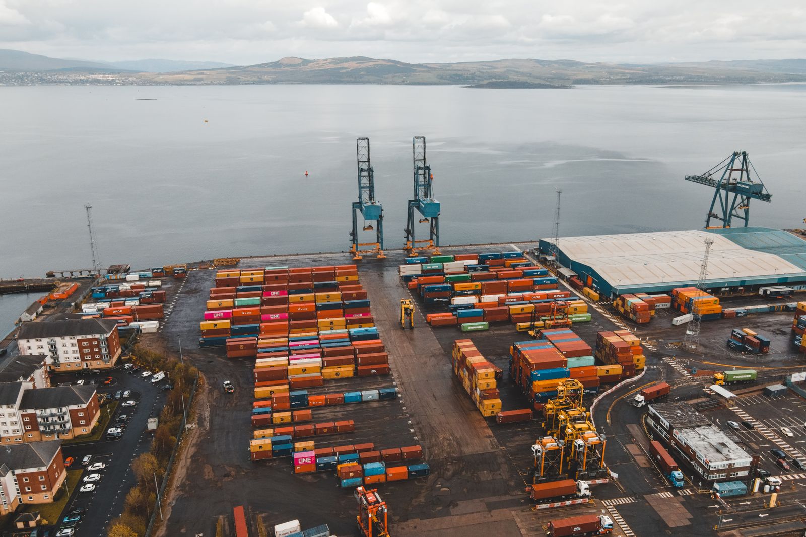 Aerial view of a container port with cranes and stacked cargo containers.