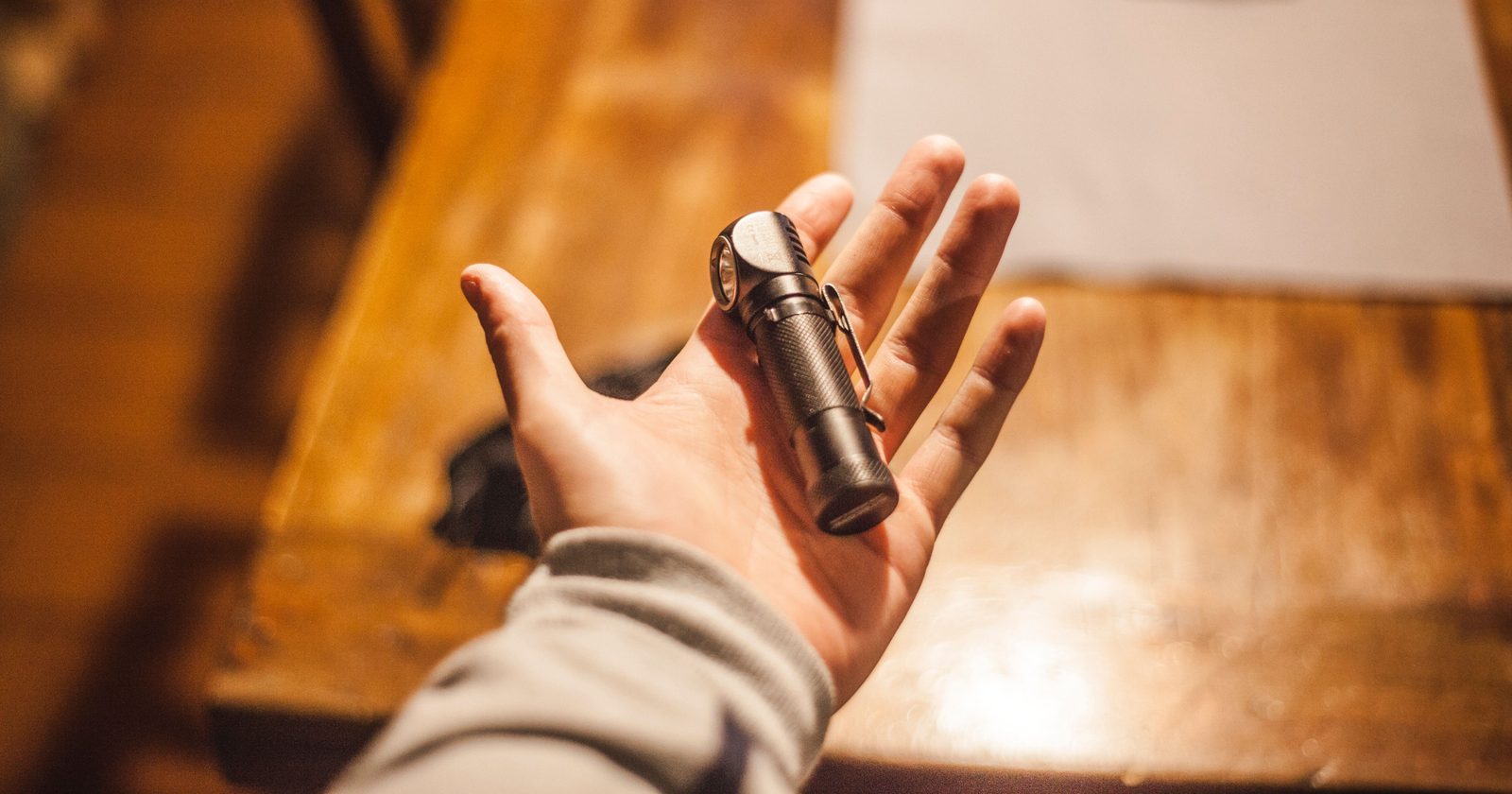 Close-up of a hand holding a flashlight on a wooden table indoors, warm lighting.