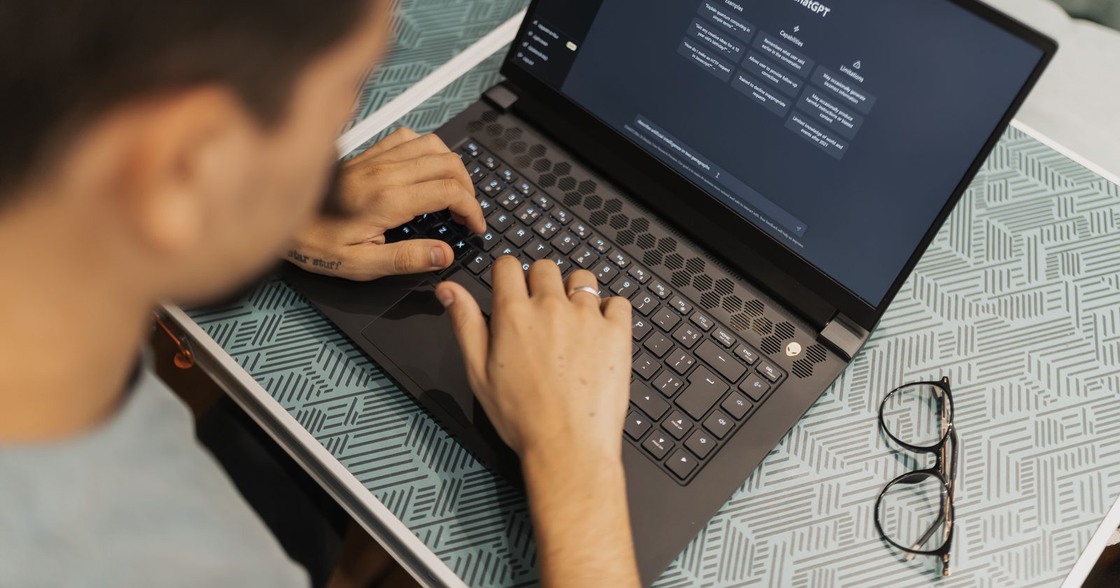 A man working on a laptop with AI software open on the screen, wearing eyeglasses.