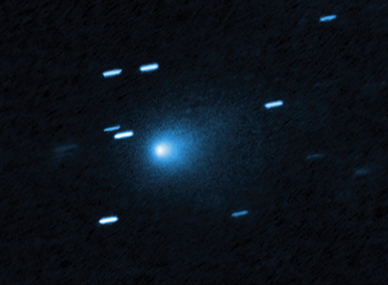 Hubble image of interstellar comet 3I/ATLAS as a blue teardrop-shaped dust coma against streaked background stars