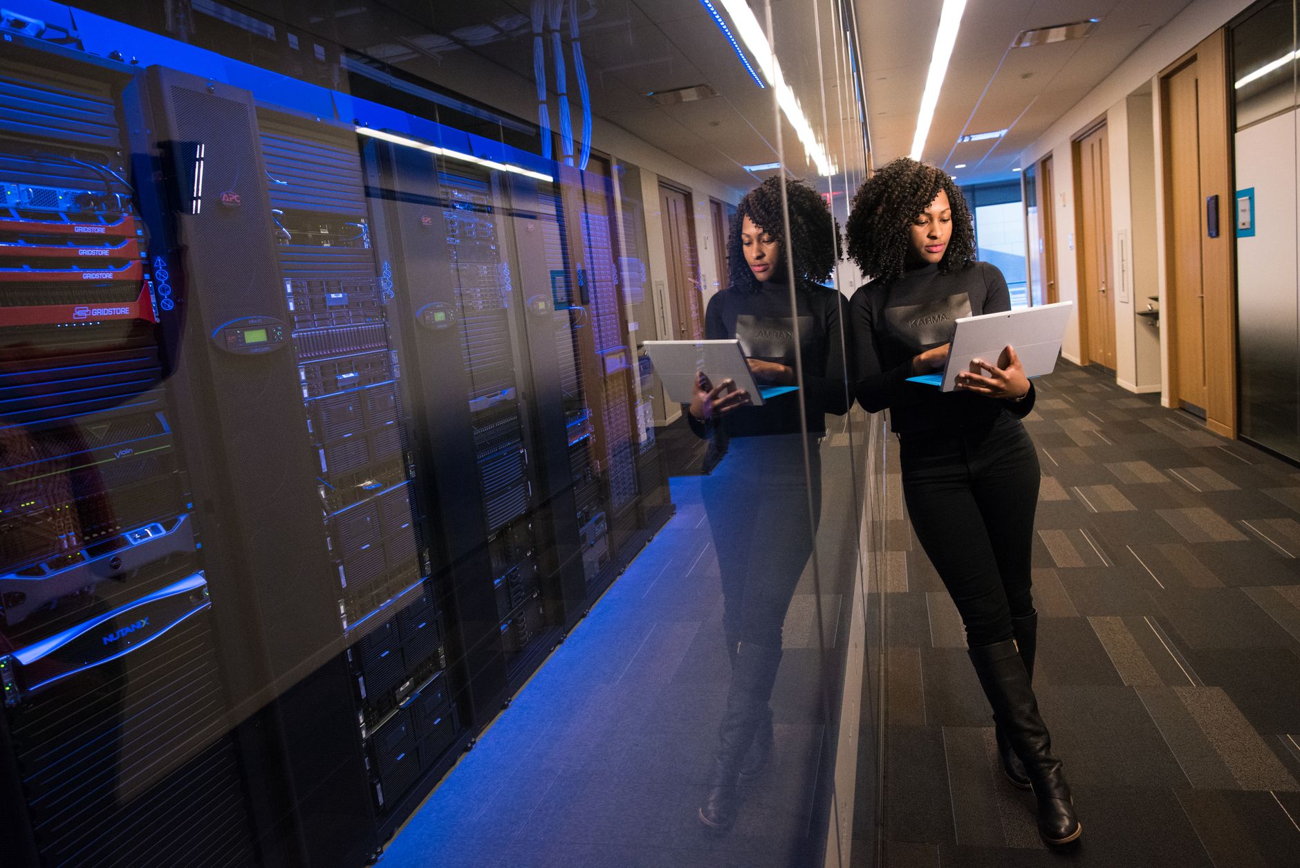 An engineer holding a tablet beside glass-fronted data-centre server racks
