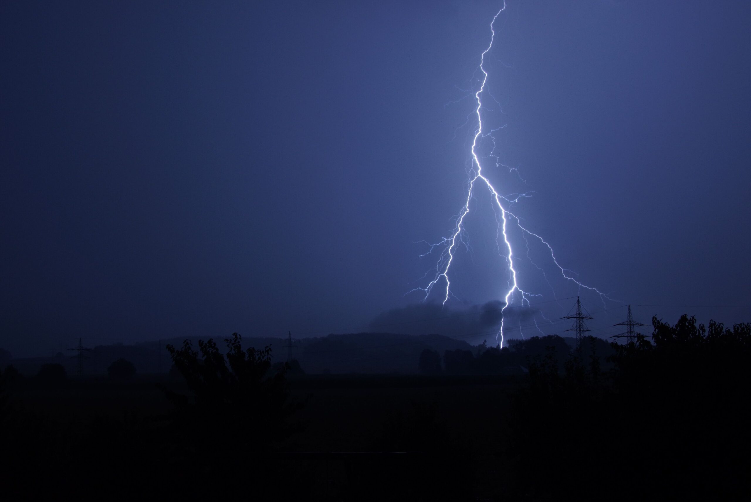 Lightning branching across a dark nighttime sky above a rural landscape