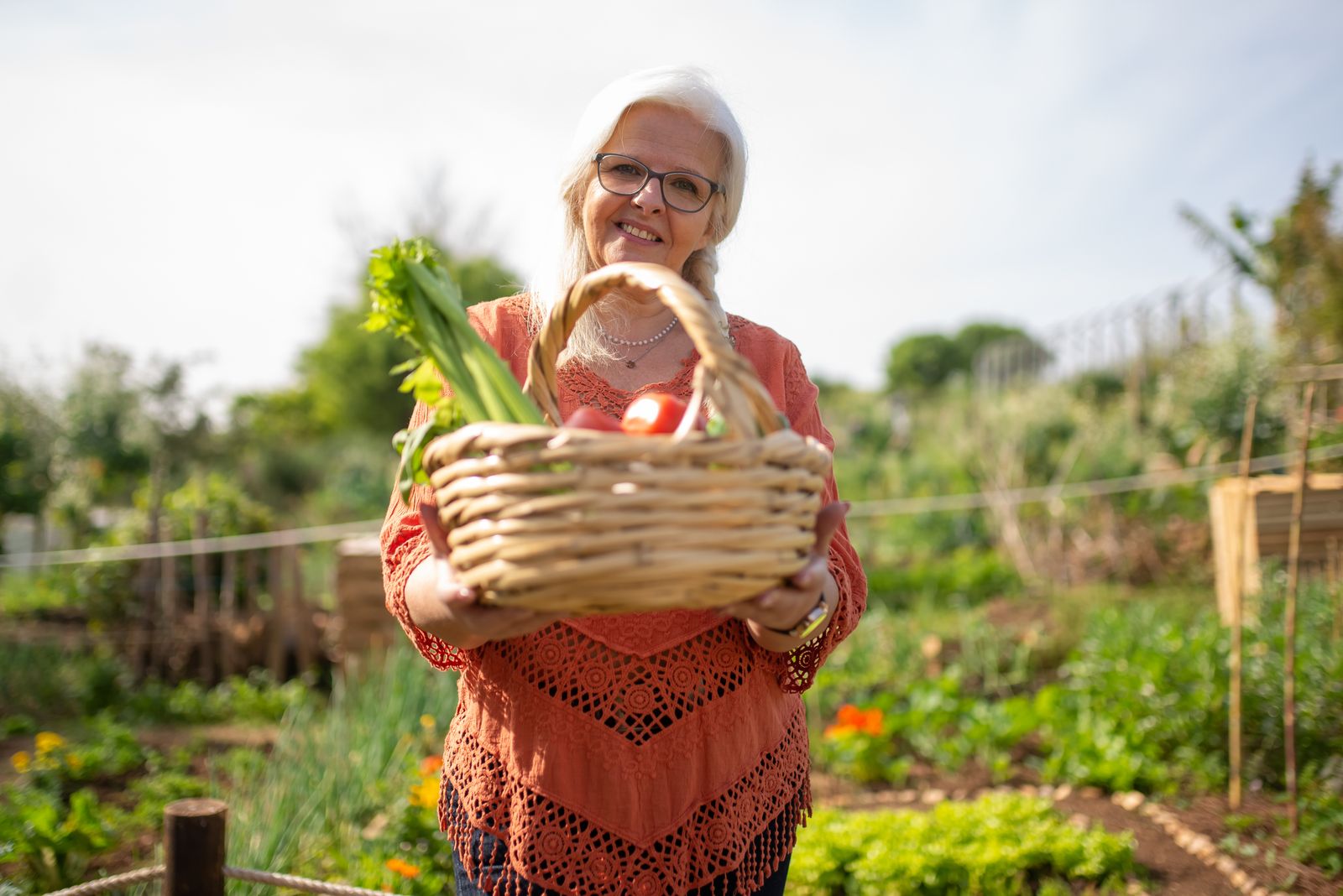 An older woman holding a basket of vegetables in a garden