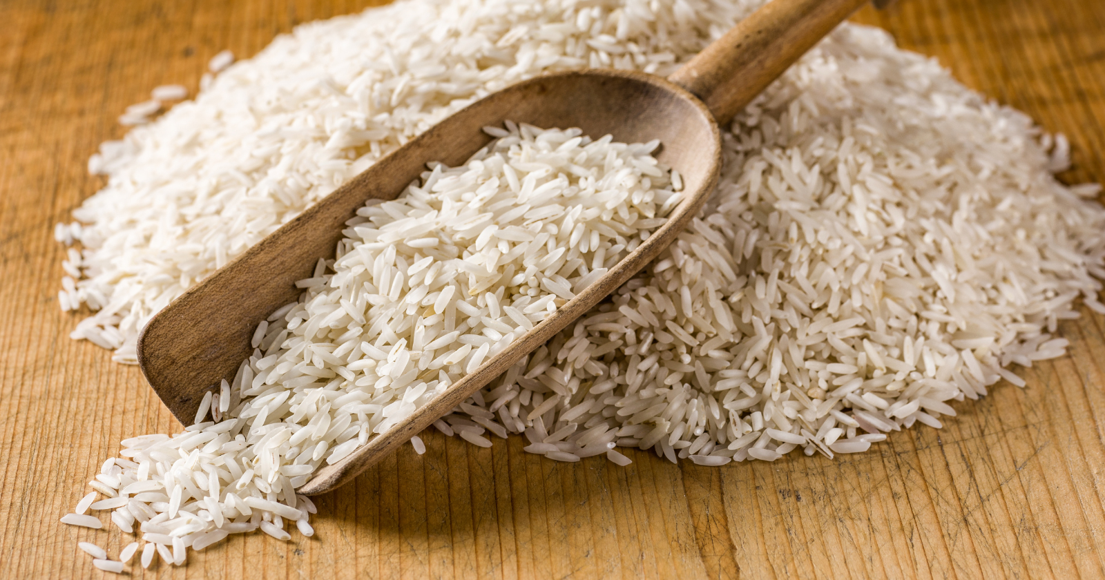 Uncooked white rice spilling from a wooden scoop