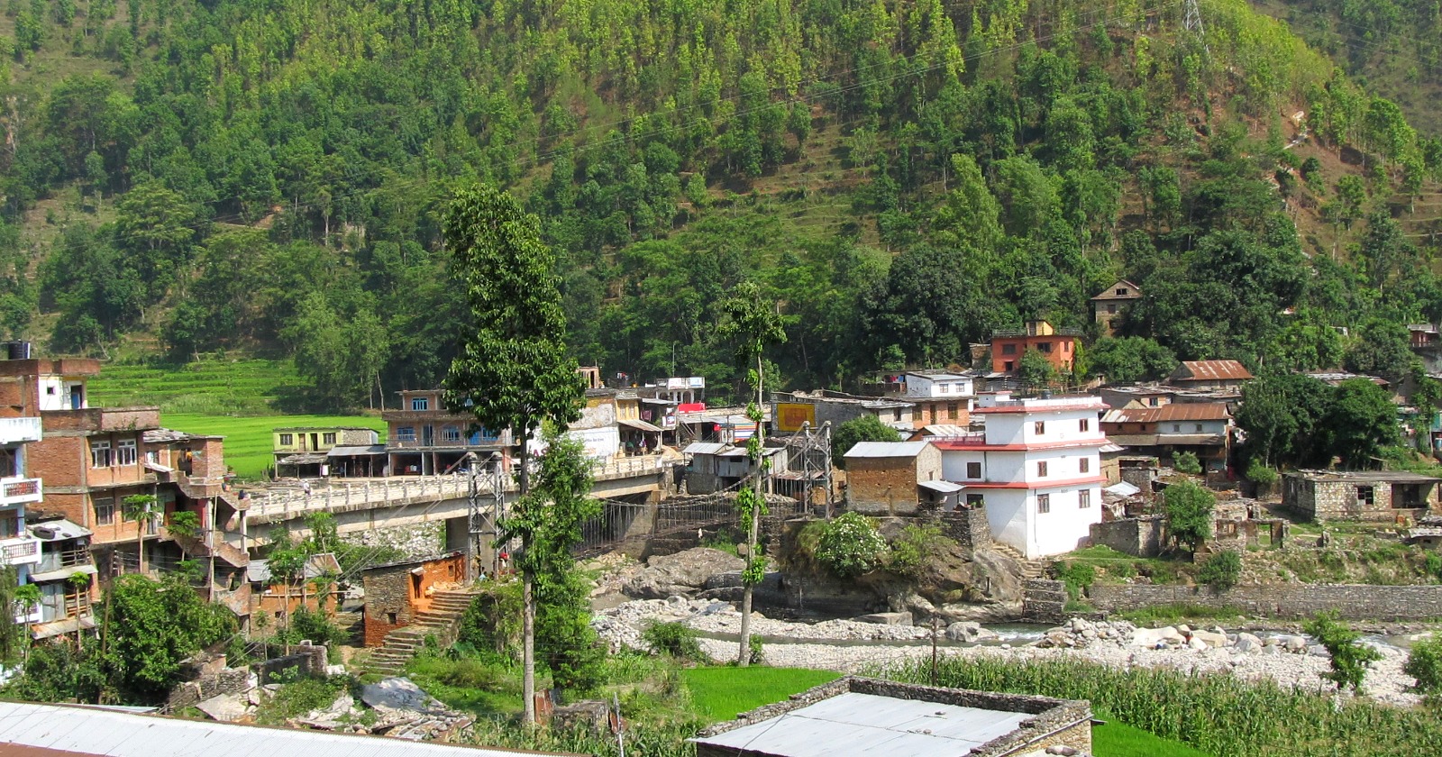 Houses and a road bridge at Betrawati, Nepal, above a wide stony river channel with the water low in it.