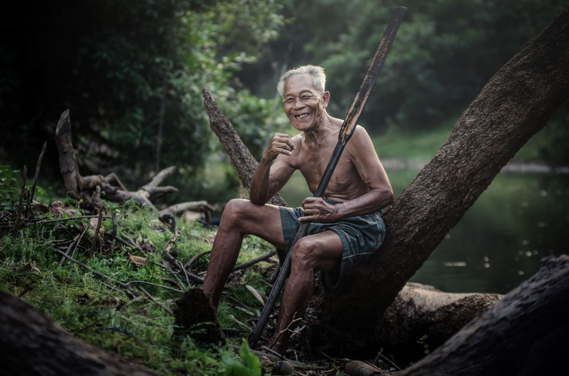 Older man sitting on a tree branch beside water