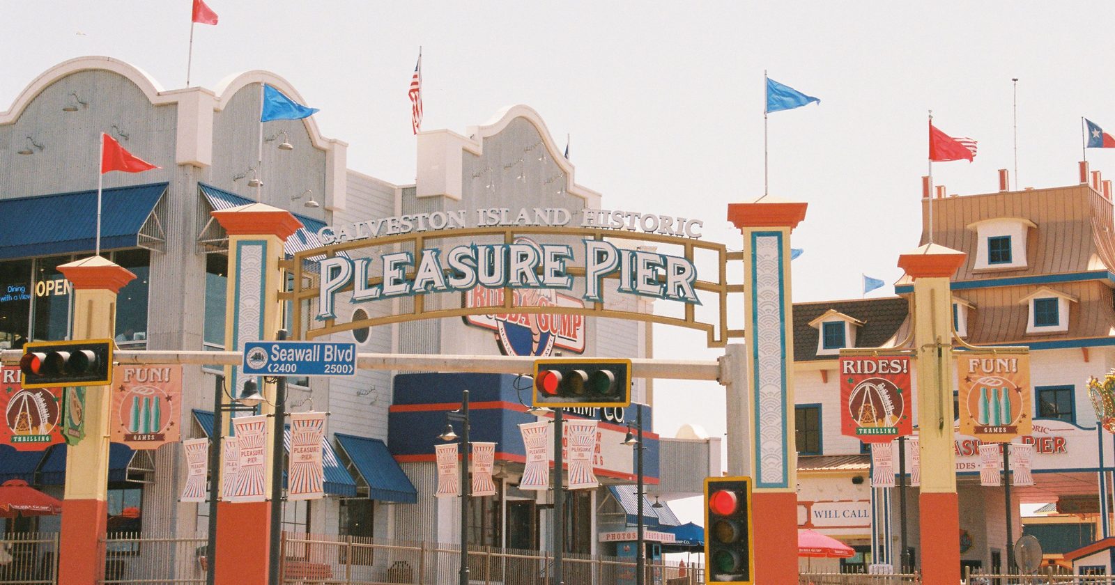 Scenic view of Galveston Island's iconic Pleasure Pier with flags and signs.