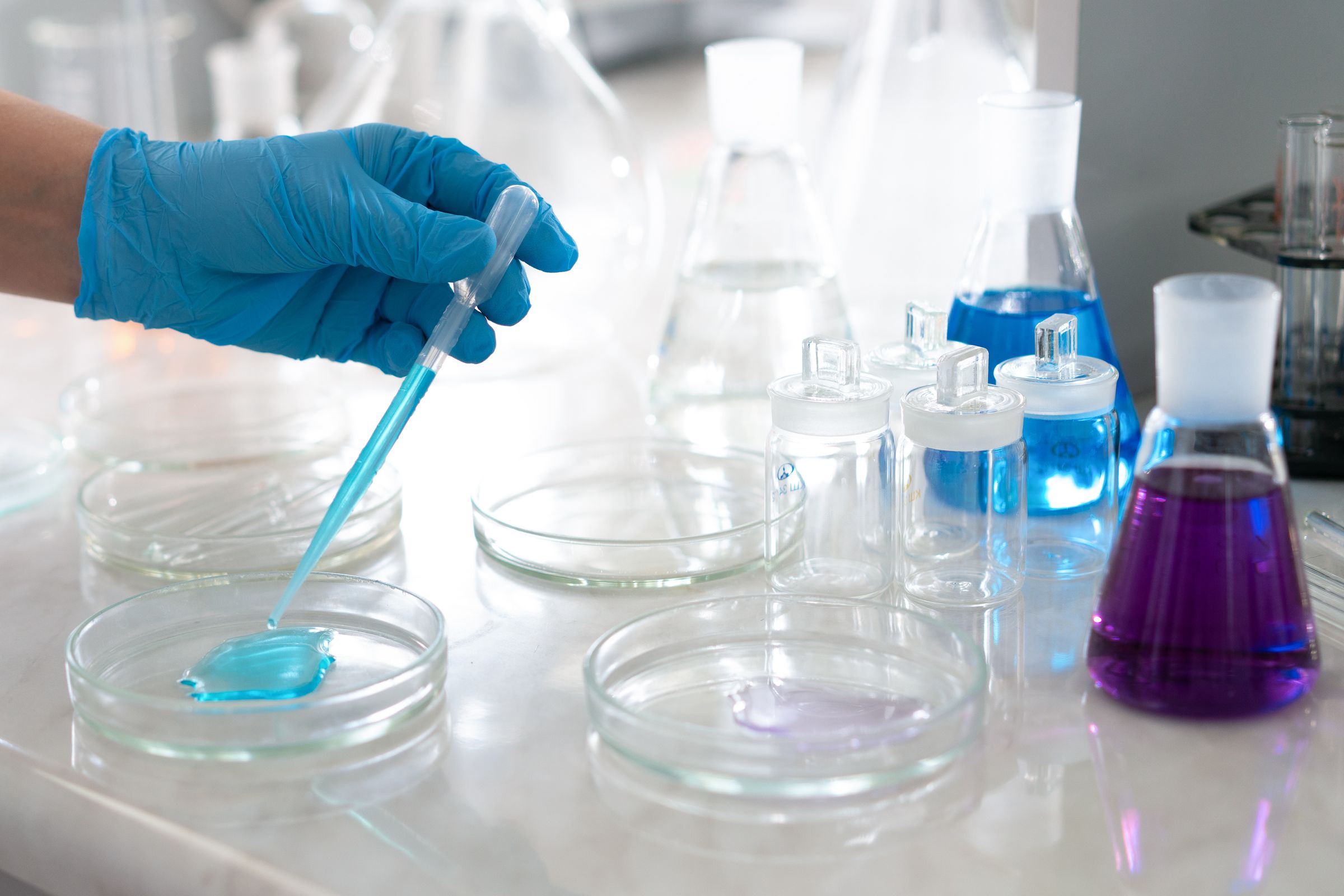 Gloved hand using a pipette over Petri dishes and laboratory glassware