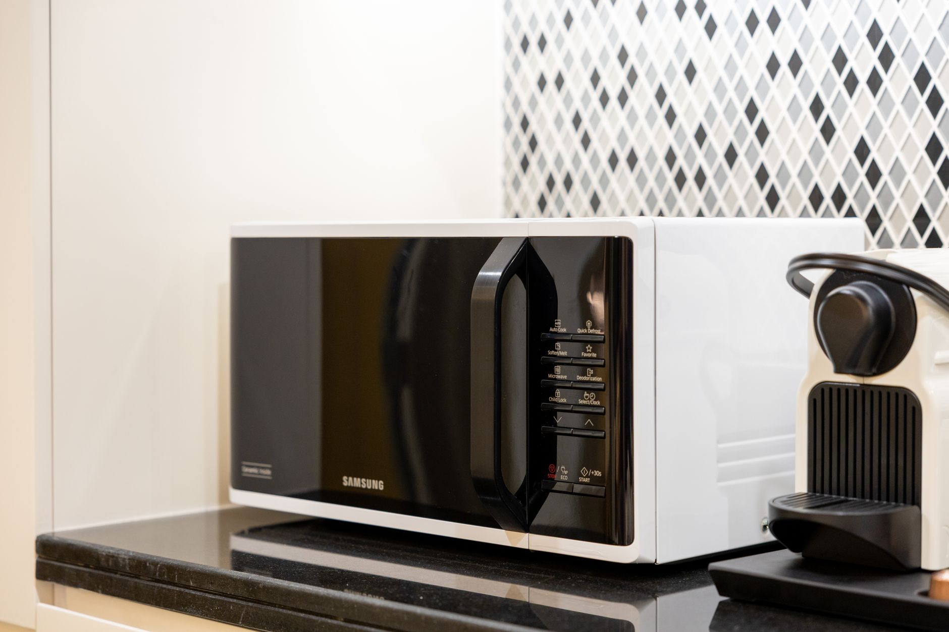 A modern black-and-white microwave oven on a kitchen counter beside a coffee machine