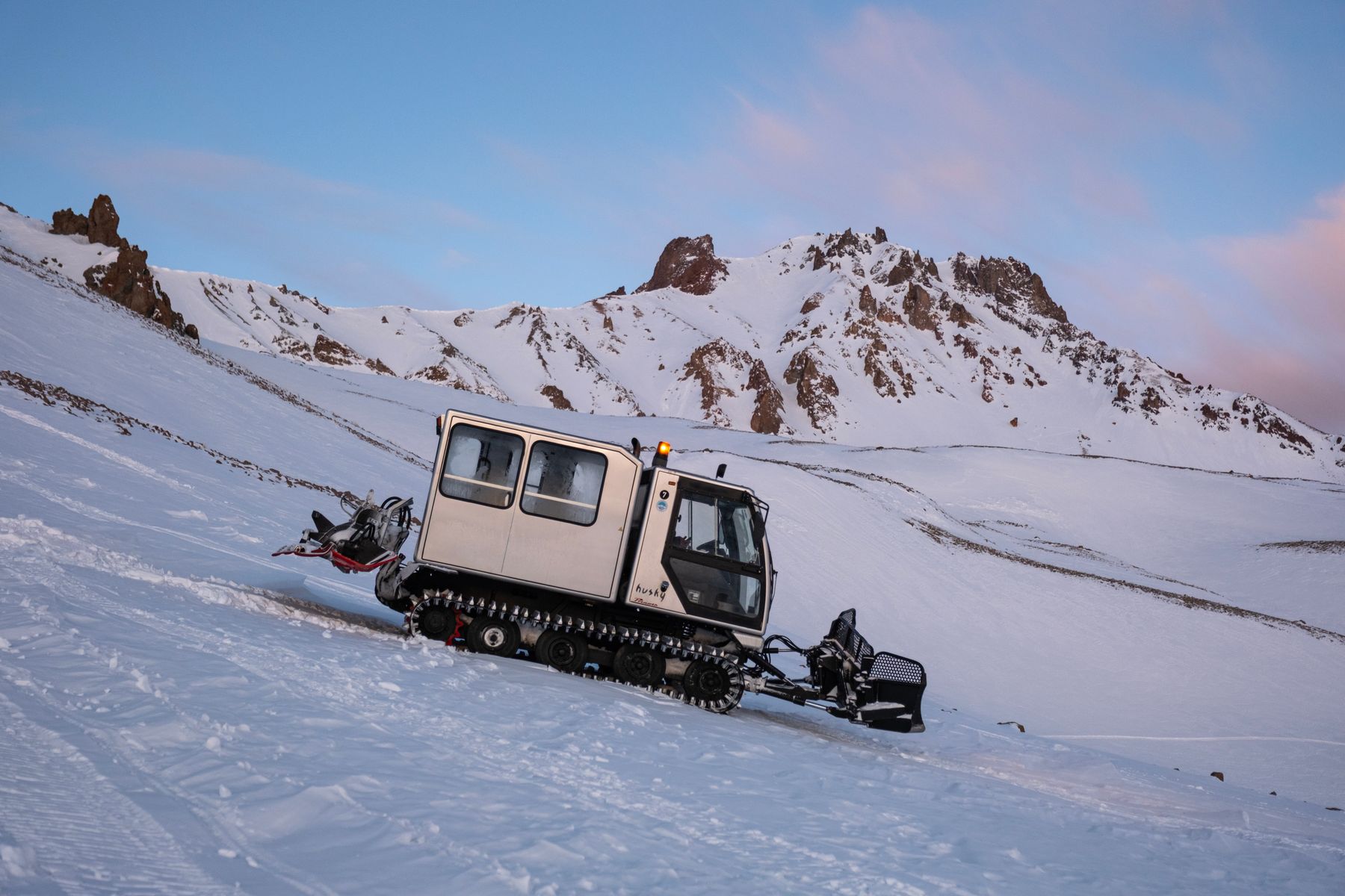 A tracked snow vehicle crossing a mountain snowfield, used as a representative image